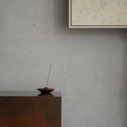 Crimson red Japanese incense holder with a lit stick on a wooden console, setting a serene mood for a meditation routine.