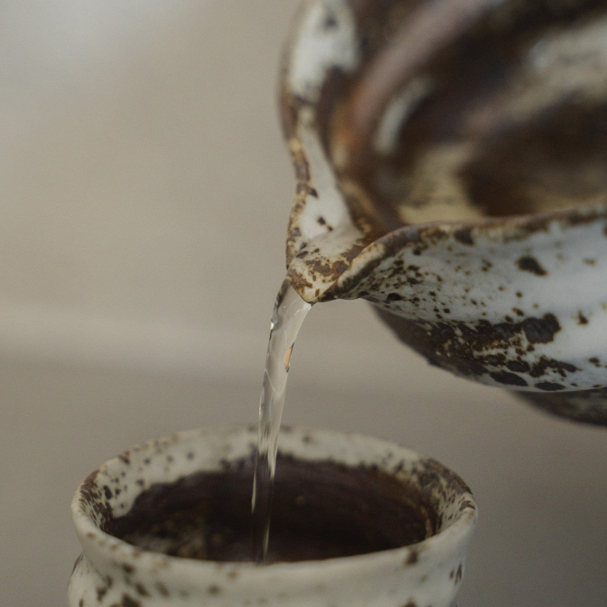 Sake fließt aus einer strukturierten japanischen Zui-Sakekaraffe in eine weiße Keramik-Sake-Tasse, um warmen Sake mühelos zu genießen