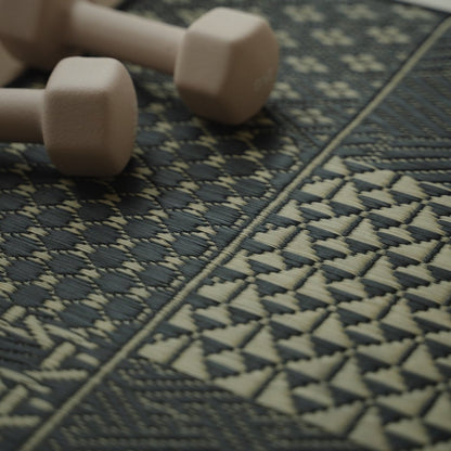 Close-up of the Japanese Tatami Yoga Mattress "Ed Plain" Black with dumbbells, highlighting intricate geometric weaves.