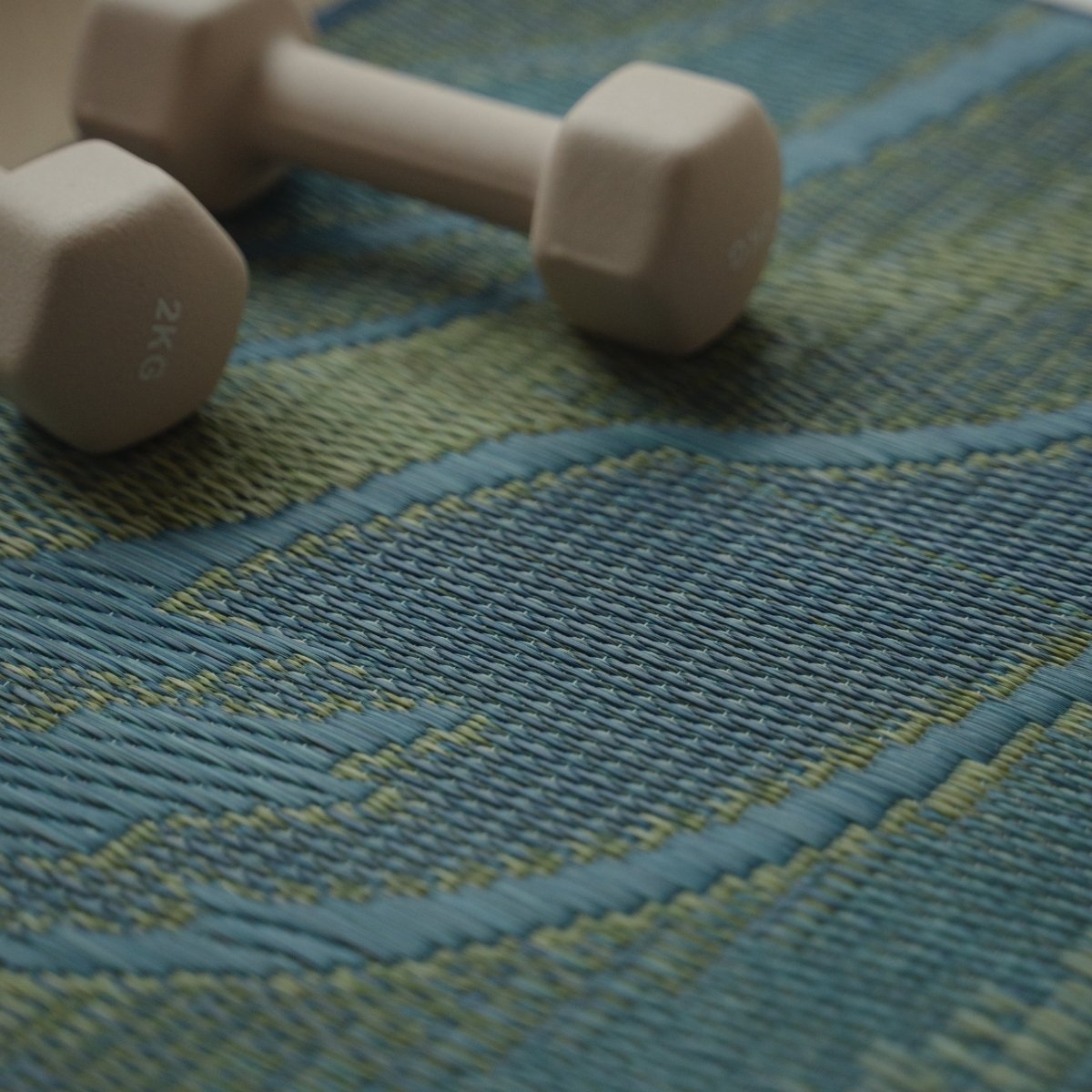 Close-up of the Japanese Tatami Yoga Mattress "Marble" Blue with a dumbbell, highlighting the woven flowing wave pattern.