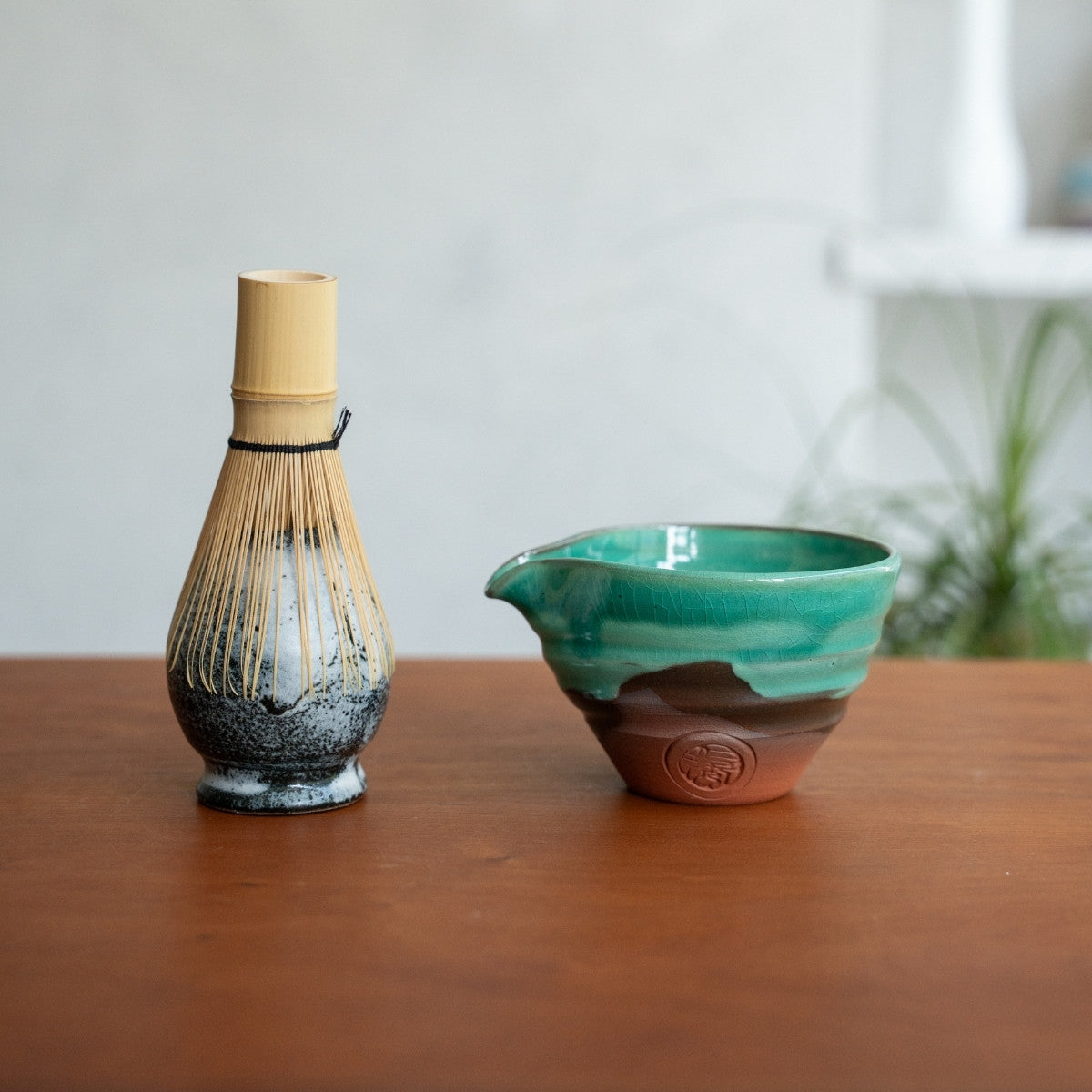 Japanese matcha whisk stand and emerald matcha bowl with spout on a wood table, ready for a daily morning tea ritual.