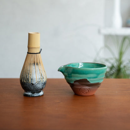 Japanese matcha whisk stand and emerald matcha bowl with spout on a wood table, ready for a daily morning tea ritual.