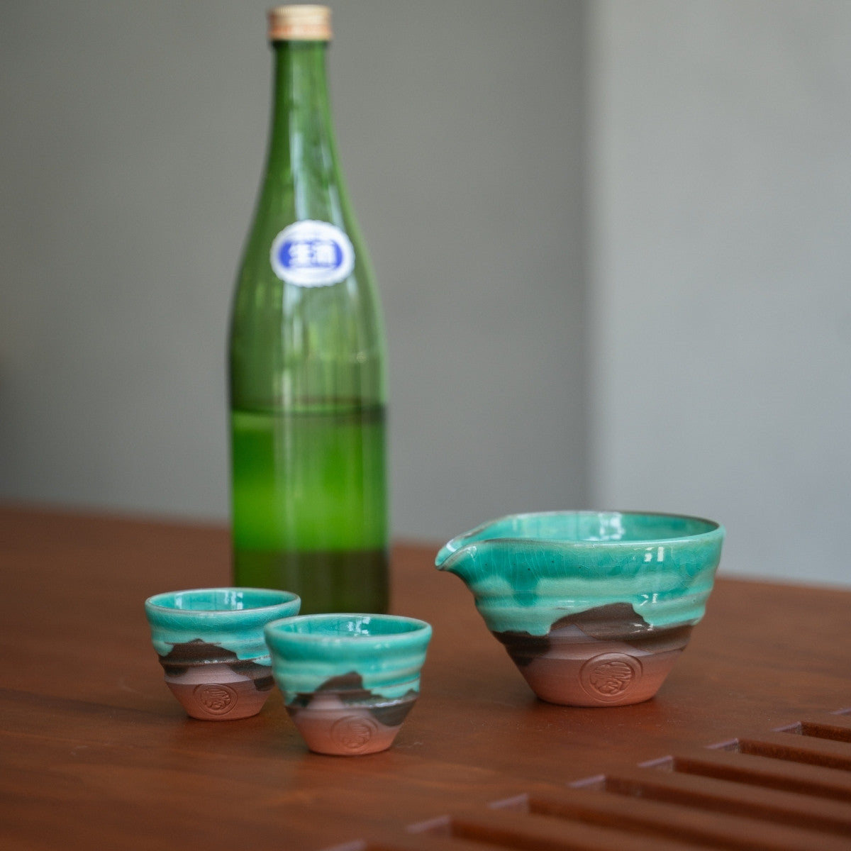 Smaragdgrünes japanisches Sake-Set (Sake-Karaffe, zwei Becher) auf einem Holztisch, bereit, einem besonderen Abendessen Eleganz zu verleihen.