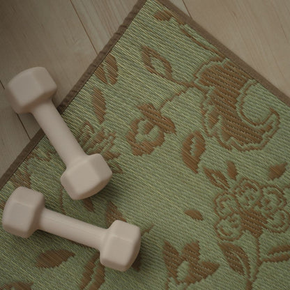 Een bovenaanzicht van een Japanse Tatami Yoga Matras "Sarasa" Beige op een houten vloer met een klein dumbbell, met de nadruk op het botanische patroon.