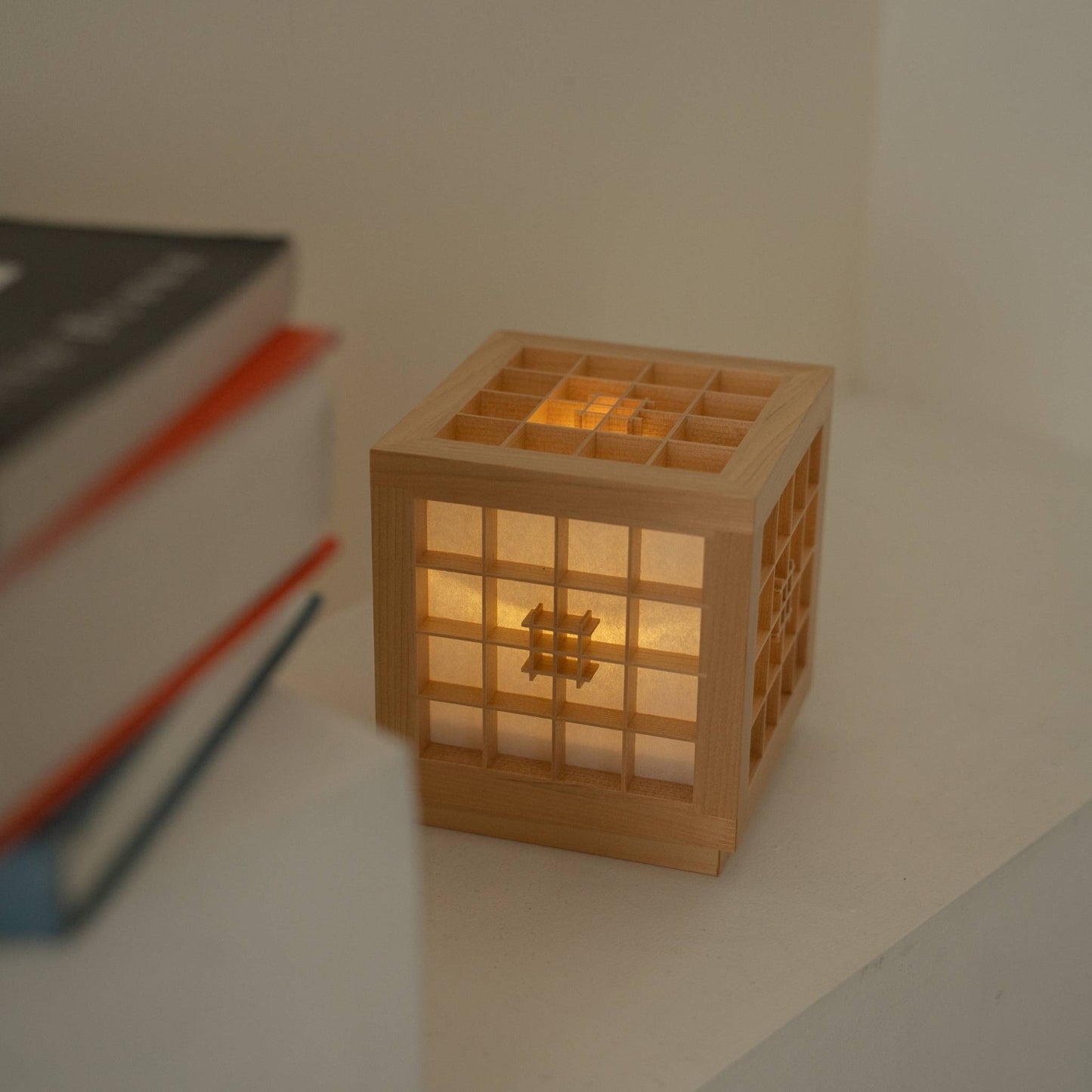 "Lampe de table japonaise en bois \"Honoka\" diffusant une lumière chaude à côté de livres, servant de lampe d'appoint sans fil confortable."