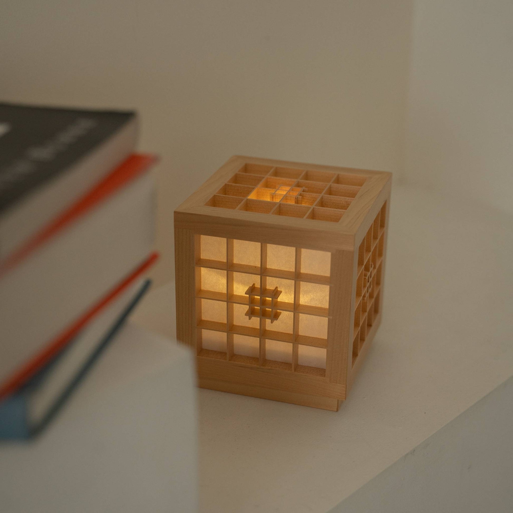 "Lampe de table japonaise en bois \"Honoka\" diffusant une lumière chaude à côté de livres, servant de lampe d'appoint sans fil confortable."