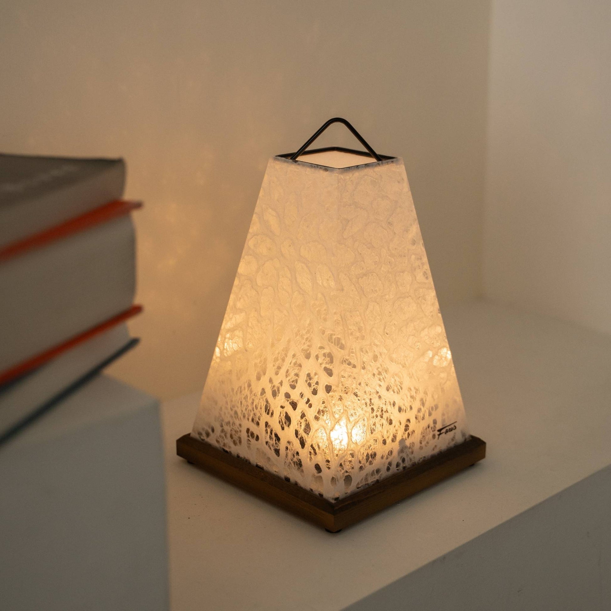 Glowing Japanese paper table lamp "Mini Akari" White serving as a cozy paper lamp accent next to books on a Japandi living room shelf.