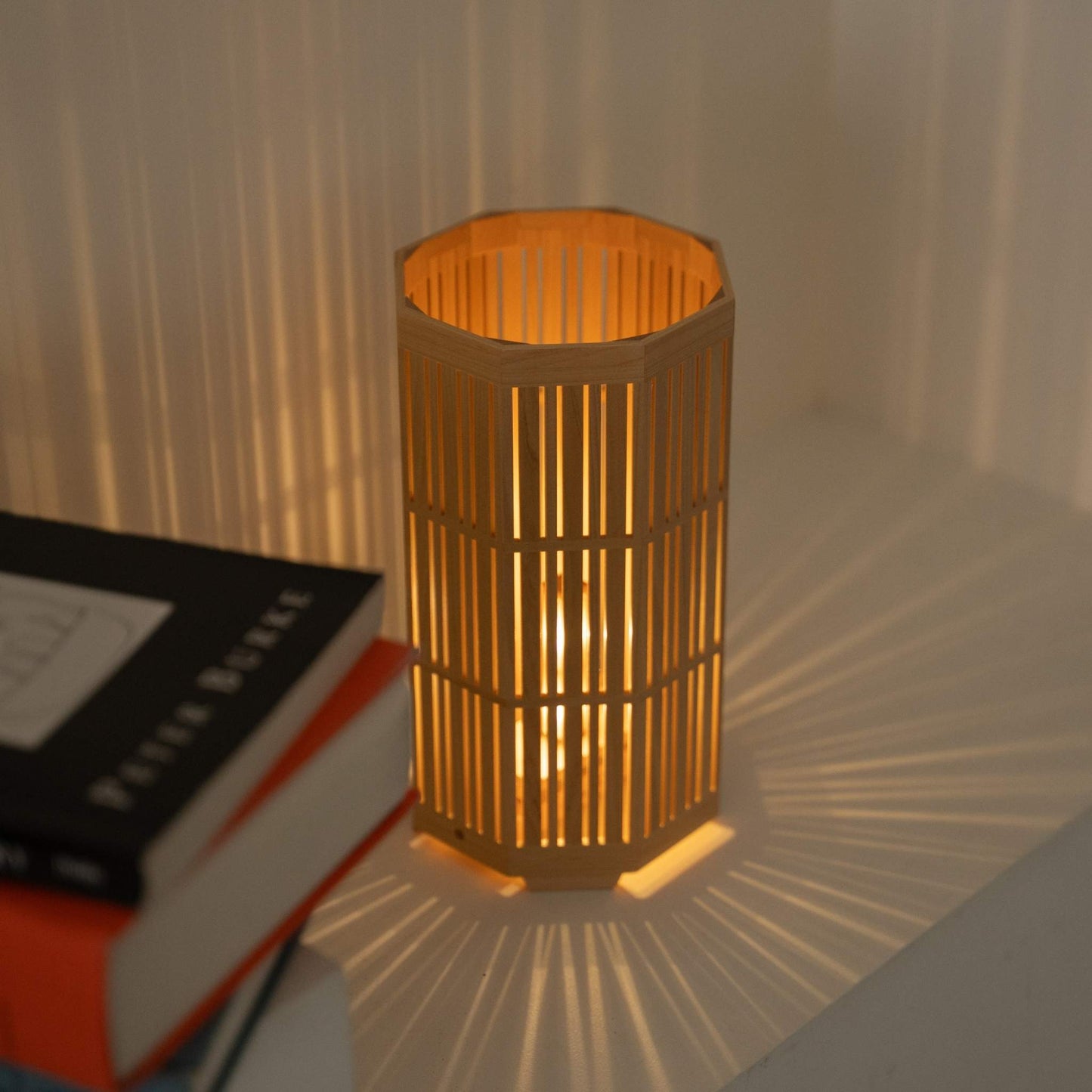 Lampe de table japonaise en bois "Kagayaki" lumineuse servant de lampe d'ambiance, projetant des ombres radiales dans une pièce de style Japandi.