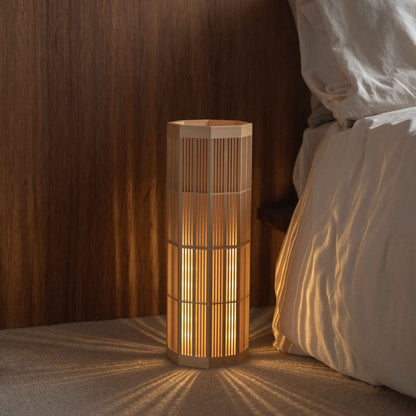 Lampe sur pied japonaise "SAN" Grand modèle en bois douillet sur le sol d'une chambre, projetant des ombres radiales apaisantes en tant que lampe d'ambiance.