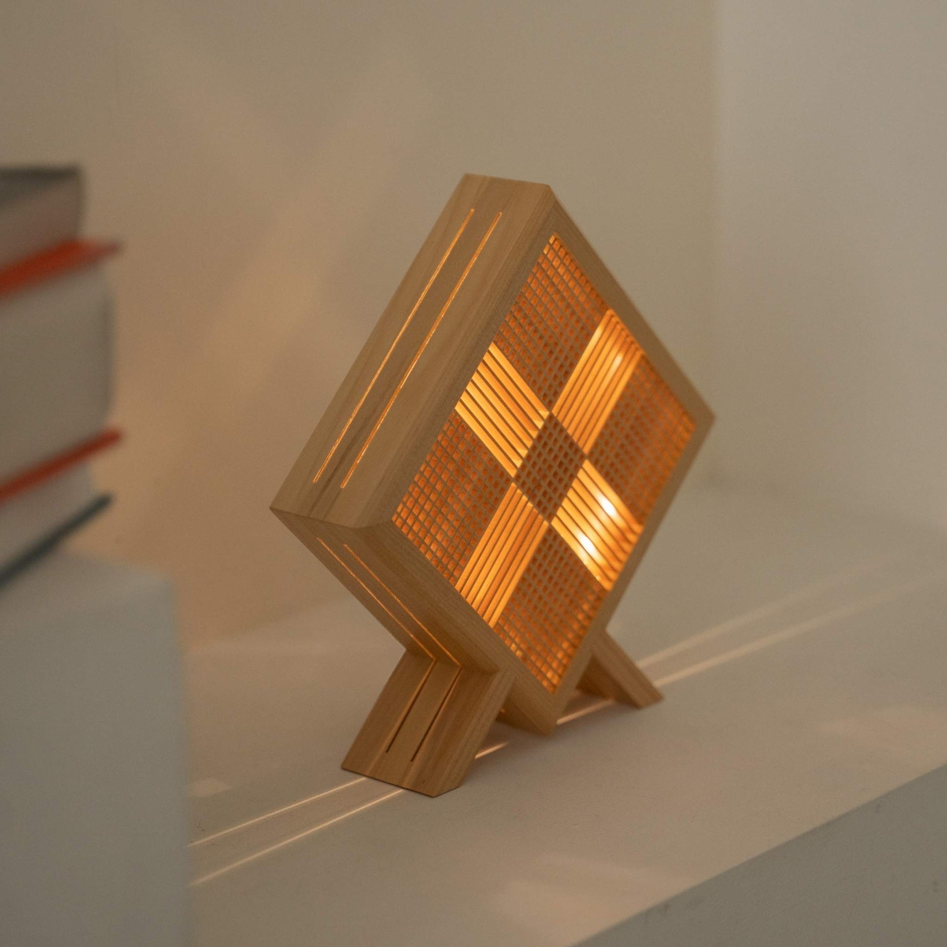 "Lampe de table japonaise Lit Kanata projetant une ombre mystique en forme de X, créant une atmosphère sereine wabi sabi sur une console Japandi."