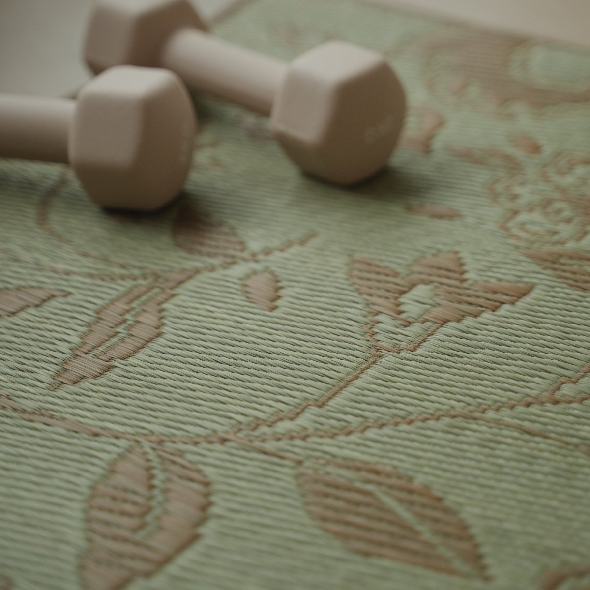 Close-up van het botanische patroon op Japanse Tatami Yogamat "Sarasa" Beige met natuurlijke matgrastextuur en een nabijgelegen halter.