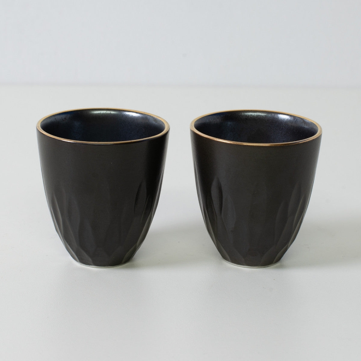 Floral carved sake cups, black porcelain - Two matte black sake cups with gold rims and textured surface