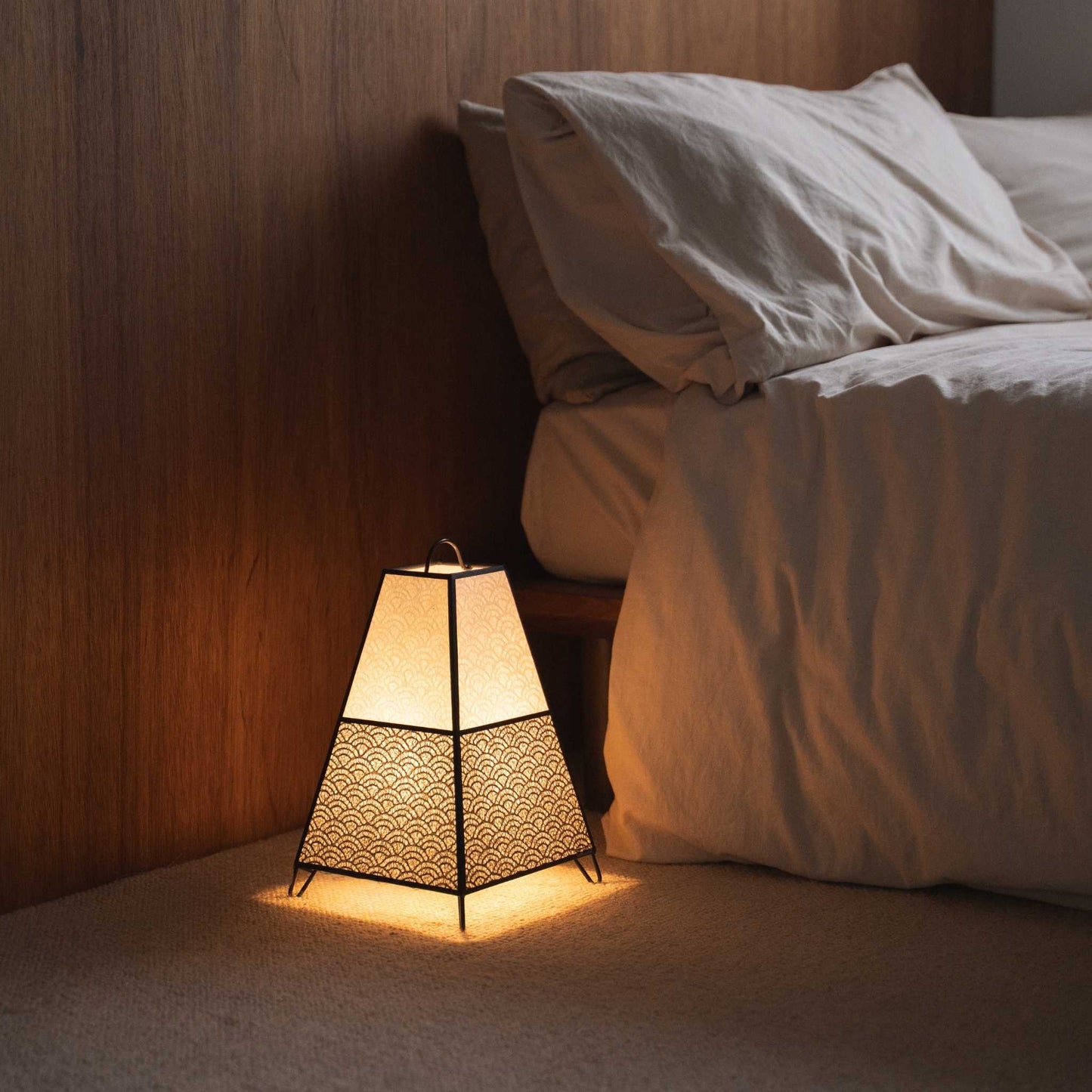 Lit Japanese floor lamp KURA Small casting intricate shadows from its paper shade as an ambient lamp in a Japandi bedroom.