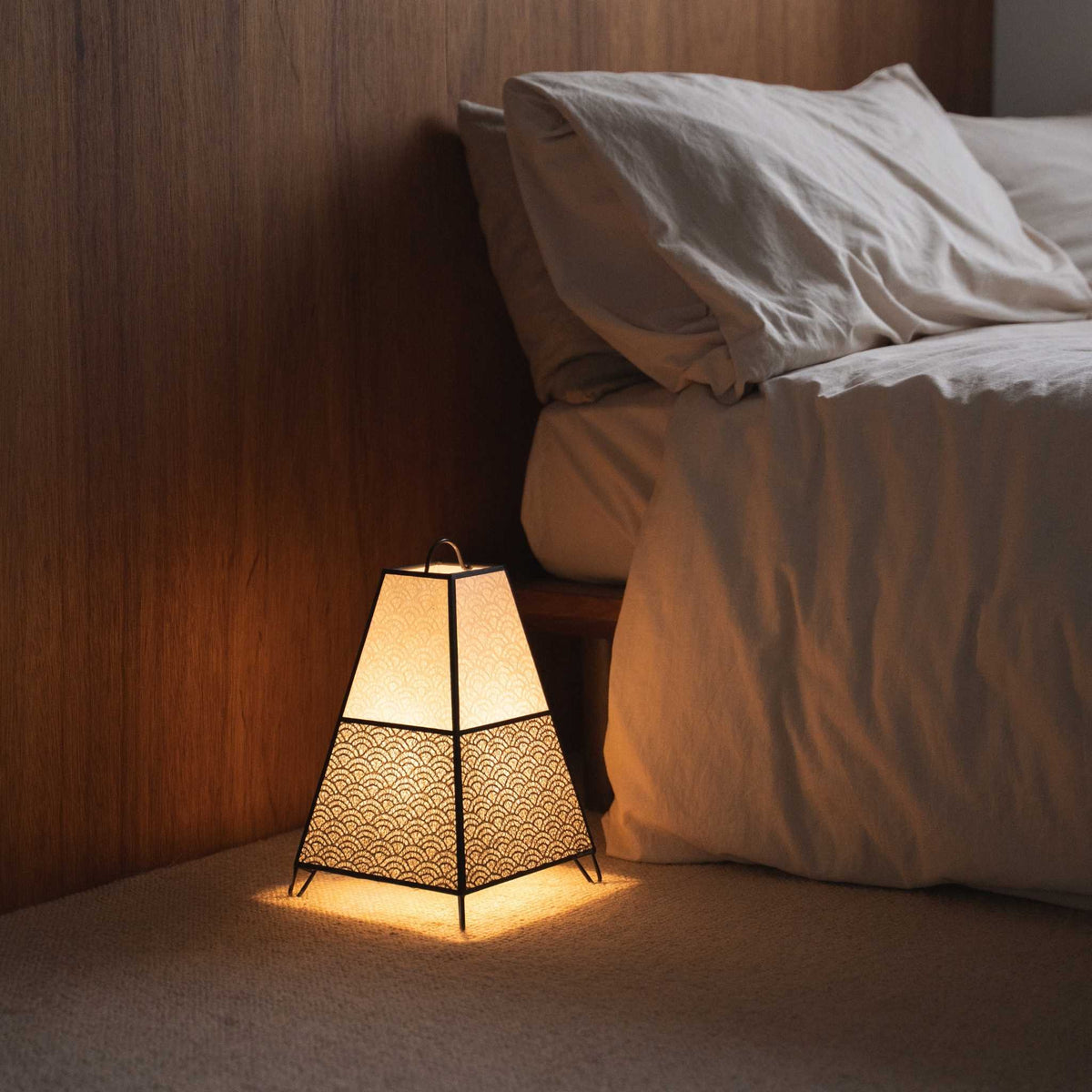 Lit Japanese floor lamp KURA Small casting intricate shadows from its paper shade as an ambient lamp in a Japandi bedroom.