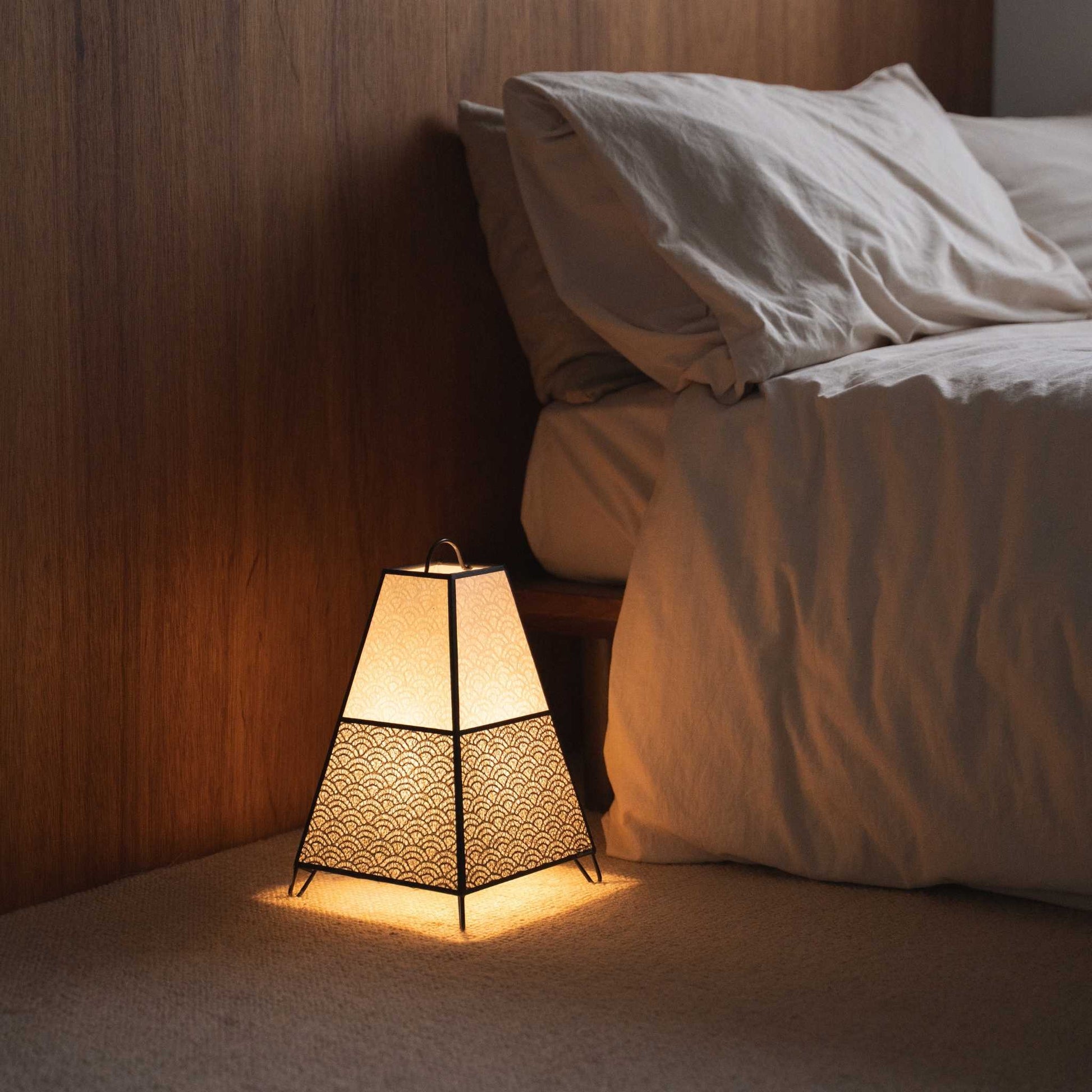 Lit Japanese floor lamp KURA Small casting intricate shadows from its paper shade as an ambient lamp in a Japandi bedroom.