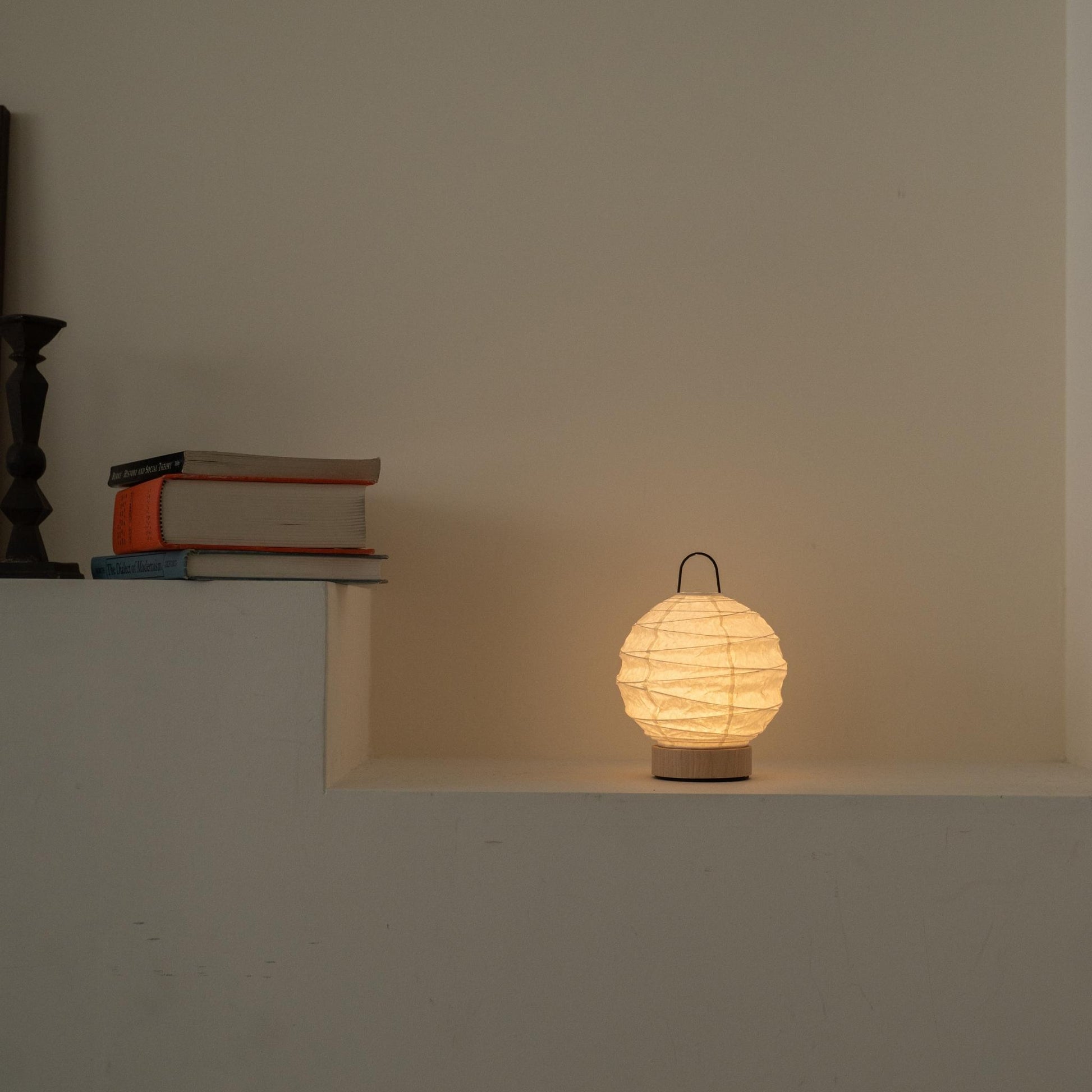 Lit round Japanese paper table lamp "Yuhi" casting a soft glow as an ambient lamp on a white Japandi style console.