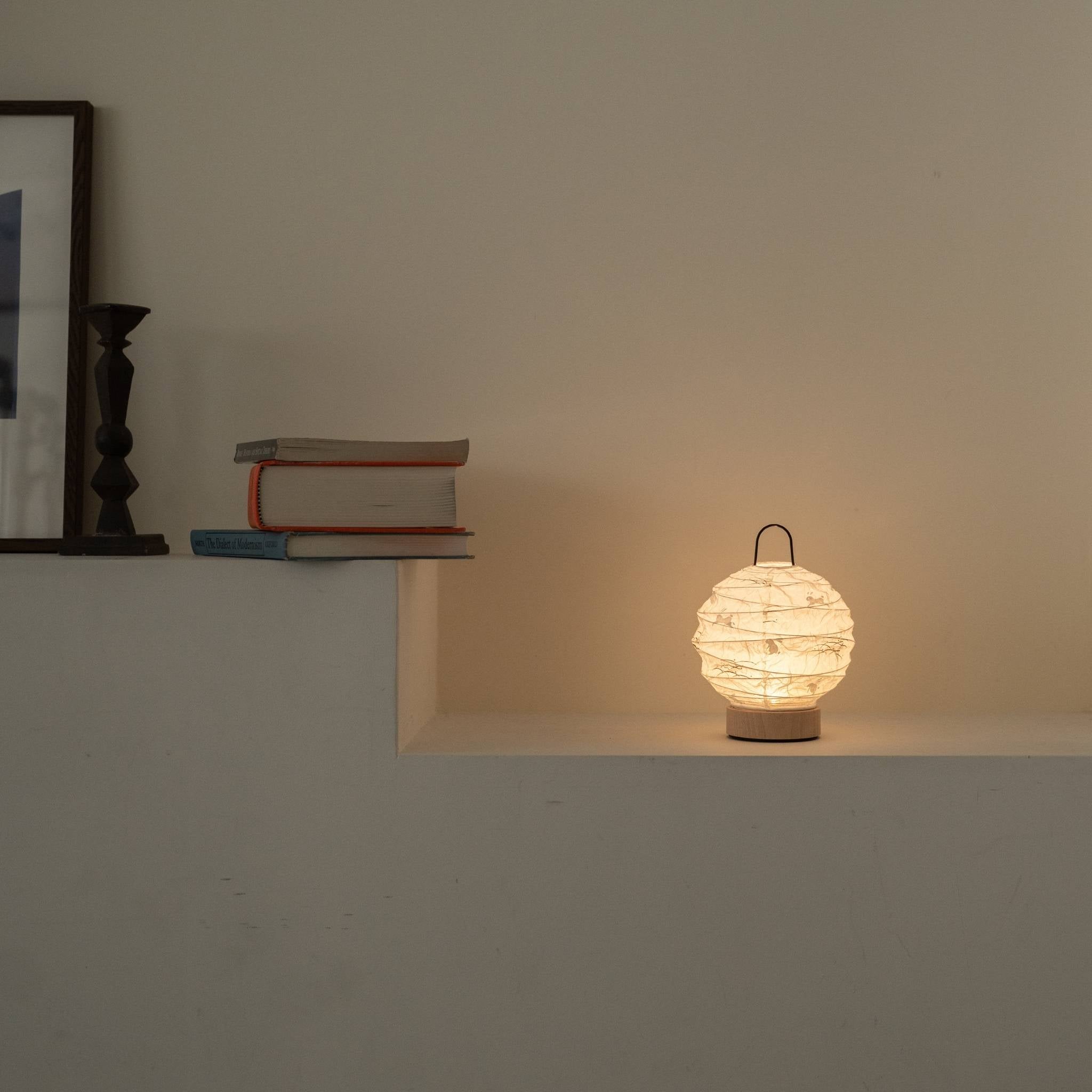 Lit round Japanese paper table lamp "Yuhi" Rabbit casting a soft glow as an ambient lamp on a white Japandi style console.