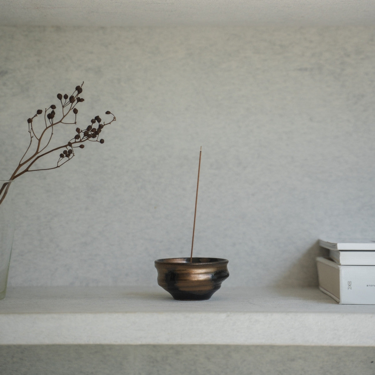 Gold and black Japanese incense burner with a lit stick on a light shelf, keeping ash contained for a calm meditation.