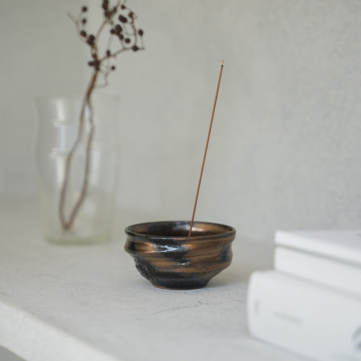 Gold-and black deep bowl Japanese incense burner with gold and black glazes on a bright shelf, adding wabi-sabi to a living room.