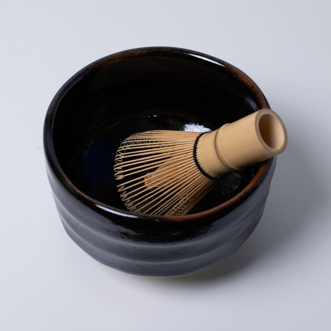 op view of "Yuzu Black" Japanese matcha bowl with a bamboo whisk, offering a dramatic contrast for green matcha tea rituals.