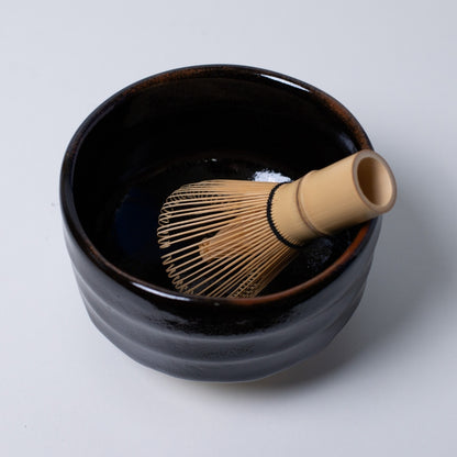 op view of "Yuzu Black" Japanese matcha bowl with a bamboo whisk, offering a dramatic contrast for green matcha tea rituals.
