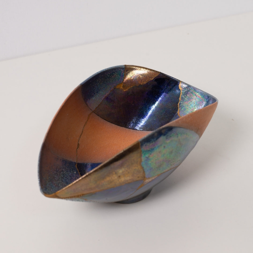 Close up looking into an iridescent kintsugi bowl featuring golden mends that celebrate wabi sabi pottery art