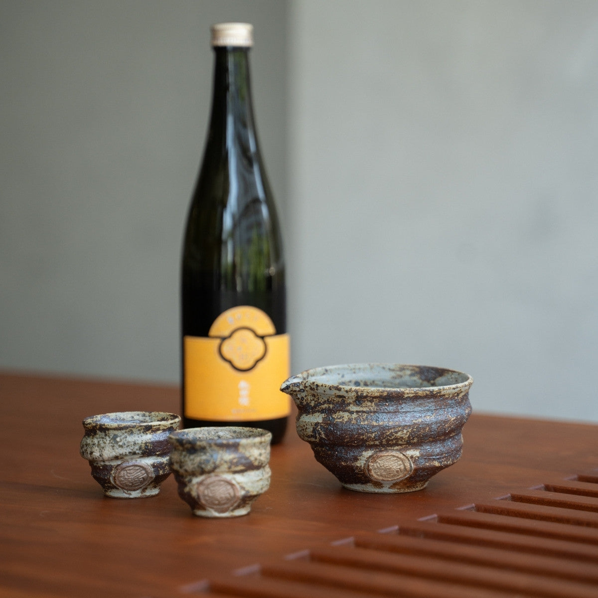 Rustikales japanisches Keramik-Sake-Set auf einem Holztisch mit einer Flasche, bereit für Erwachsene, um einen entspannten Abend zu genießen.
