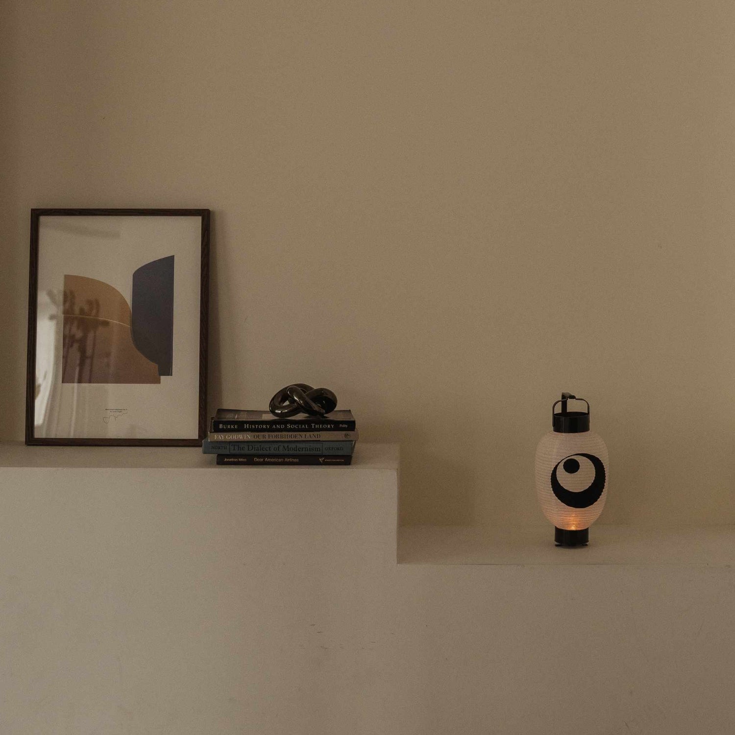Standing Japanese lantern with moon and star motif placed on a white shelf next to books and art frame.