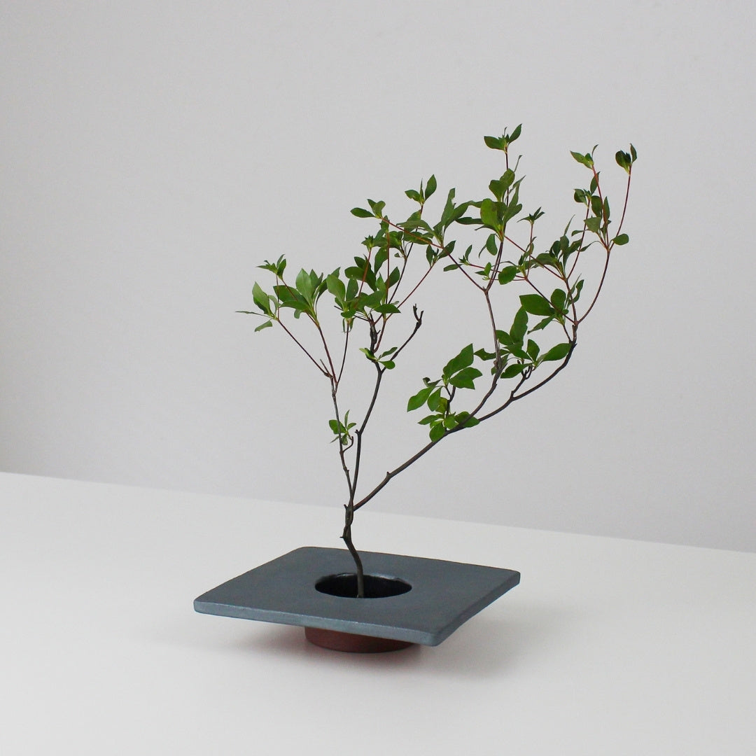 A minimalist iron ikebana vase inspired by traditional Japanese roof tiles, featuring a kenzan (flower frog) for arranging flowers.