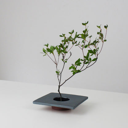 A minimalist iron ikebana vase inspired by traditional Japanese roof tiles, featuring a kenzan (flower frog) for arranging flowers.