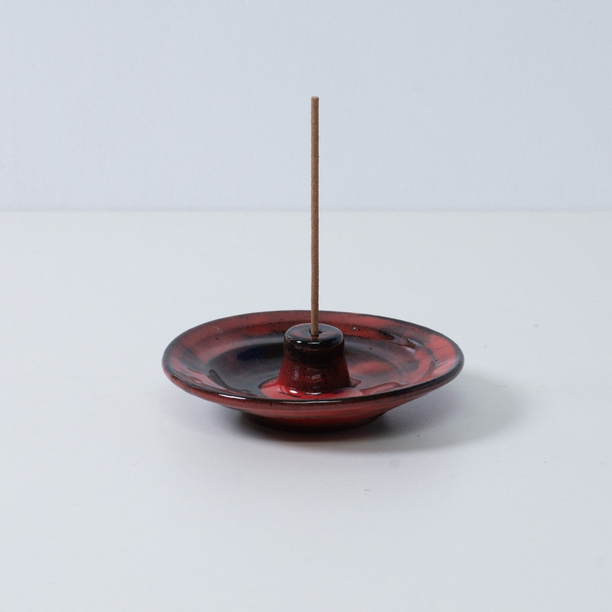 Standalone Japanese incense holder "Nobel Red" pottery tray with a single stick, showing the crimson and black glaze, Japan.