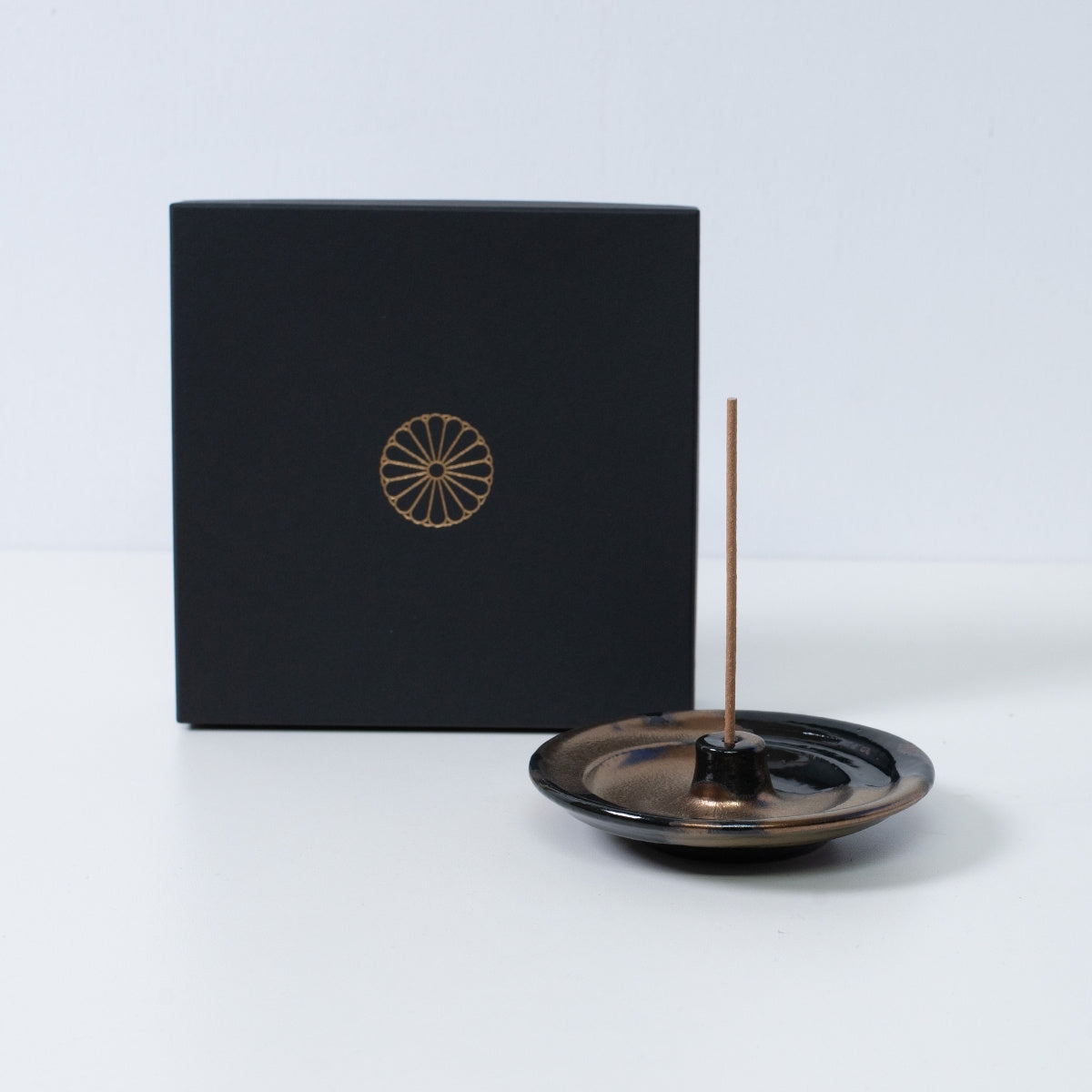Gold and black Japanese incense holder "Zen" pottery with a stick next to a black gift box with a gold chrysanthemum crest, made in Japan.