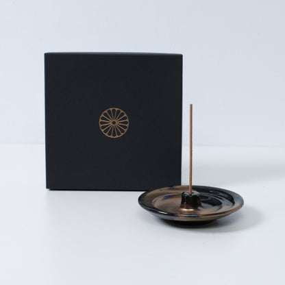 Gold and black Japanese incense holder "Zen" pottery with a stick next to a black gift box with a gold chrysanthemum crest, made in Japan.