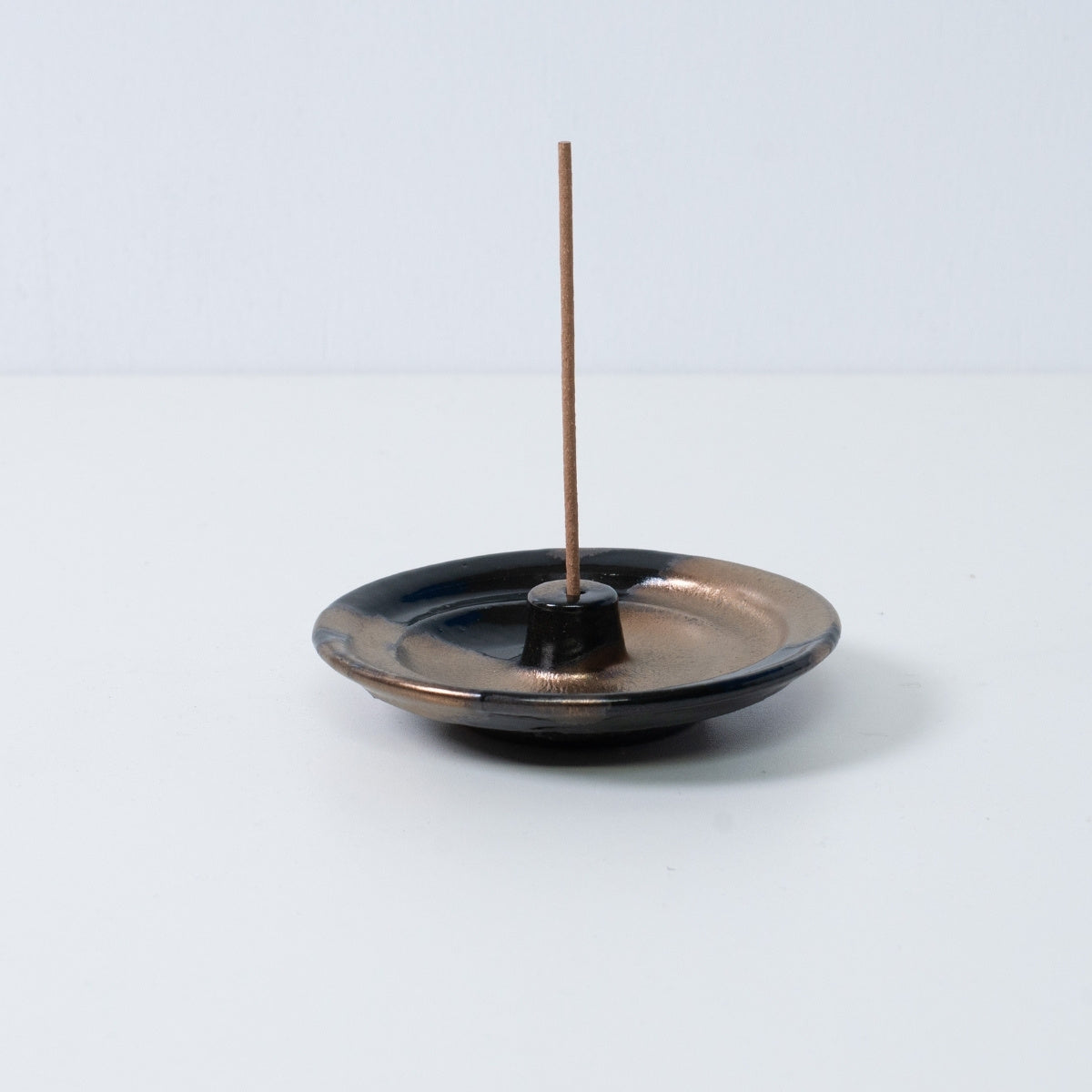 Standalone Japanese incense holder "Zen" pottery tray with a single stick, showing the gold and black glaze, from Japan.