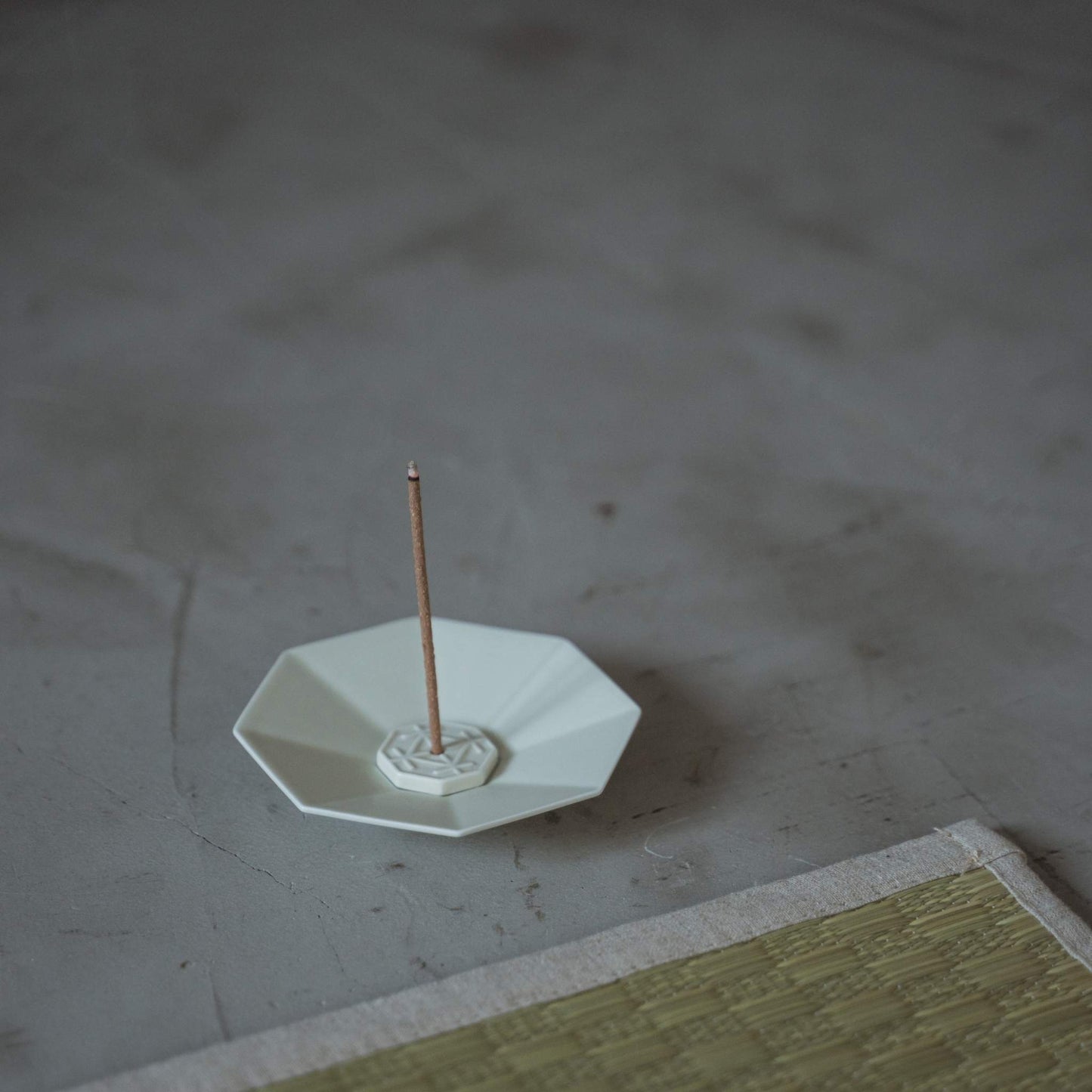 White octagon porcelain japanese incense burner holding a lit stick in a minimalist zen meditation space.