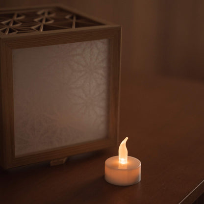 Wooden kumiko lantern cover standing next to a small lit led tea light candle on a table demonstrating how to use it