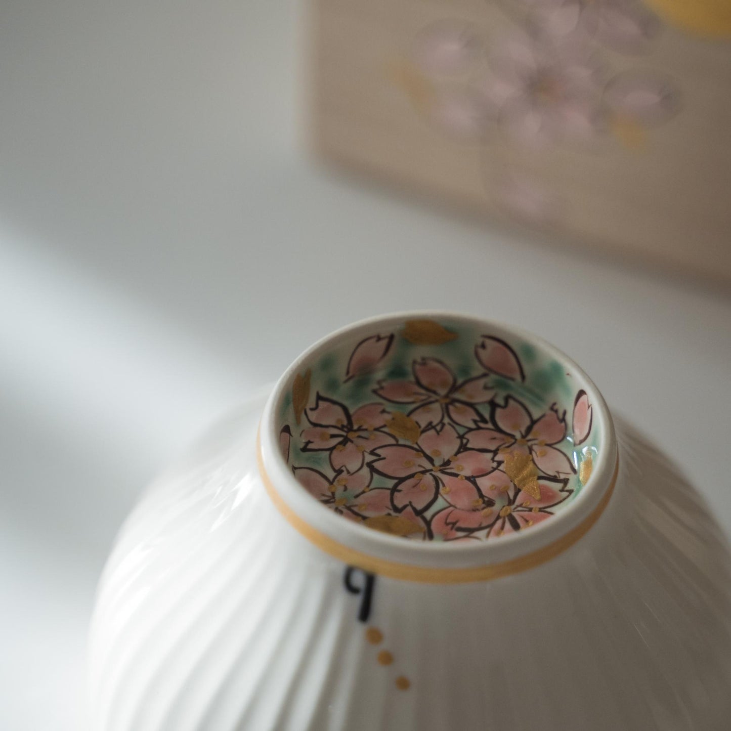 Upside down white matcha bowl displaying pink cherry blossoms painted inside the foot ring.