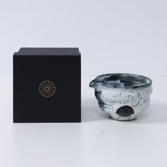 White and black Japanese matcha bowl with spout "Creative Cloud "pottery beside a black gift box with a gold chrysanthemum crest, from Japan.