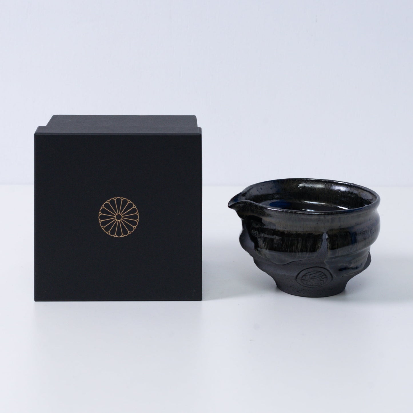 Japanse matcha kom met tuit "Dignity Blue" aardewerk naast een zwarte geschenkdoos met een gouden chrysant-embleem, uit Japan.