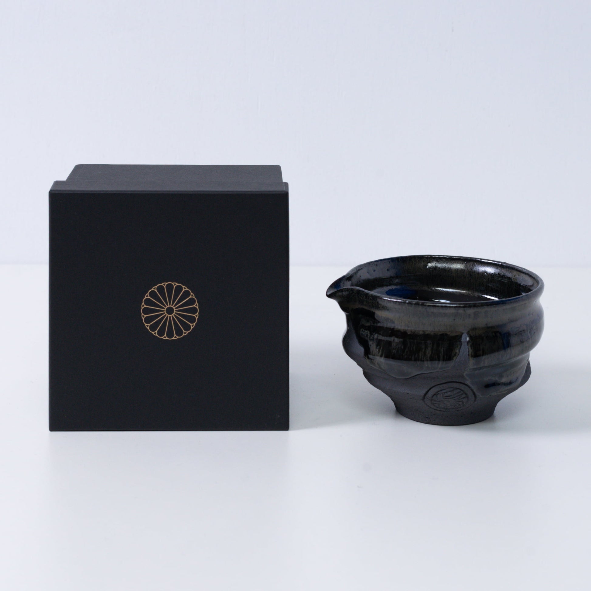 Japanse matcha kom met tuit "Dignity Blue" aardewerk naast een zwarte geschenkdoos met een gouden chrysant-embleem, uit Japan.