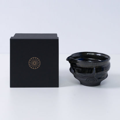 Japanse matcha kom met tuit "Dignity Blue" aardewerk naast een zwarte geschenkdoos met een gouden chrysant-embleem, uit Japan.