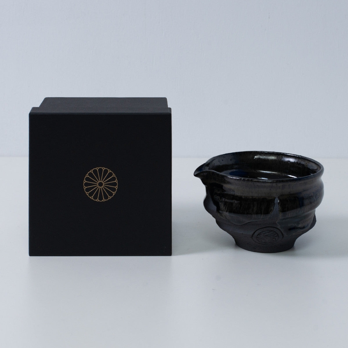 Japanese matcha bowl with spout "Dignity Blue" pottery beside a black gift box with a gold chrysanthemum crest, from Japan.