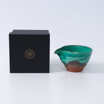 Japanse matcha kom met tuit "Smaragd" aardewerk naast een zwarte geschenkdoos met een gouden chrysant-embleem, gemaakt in Japan.