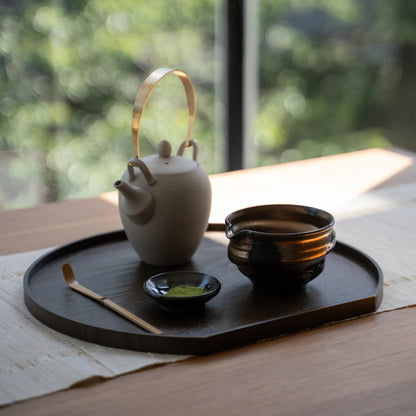 Japanese matcha bowl with spout and tea tools arranged on a dark tray by a sunny window for a peaceful authentic tea time.