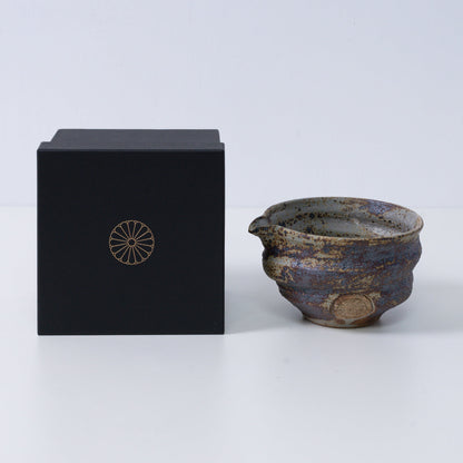 Rustieke bruine Japanse matchakom met tuit "Sakigake" aardewerk naast een zwarte geschenkdoos met een gouden chrysantenembleem, gemaakt in Japan.