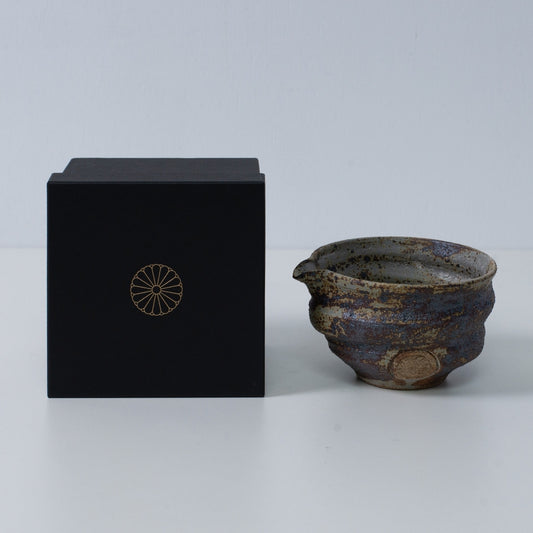 Rustic brown Japanese matcha bowl with spout "Sakigake" pottery next to a black gift box with a gold chrysanthemum crest, made in Japan.