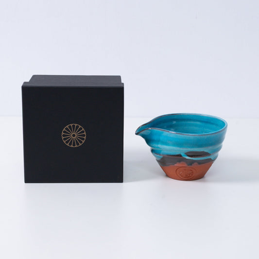 Turquoise blue Japanese matcha bowl with spout "Soku Blue" pottery beside a black gift box with a gold chrysanthemum crest, made in Japan.