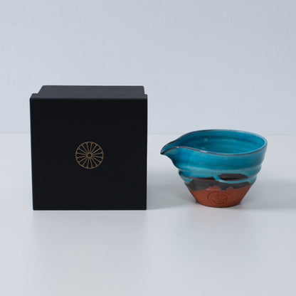 Turquoise blue Japanese matcha bowl with spout "Soku Blue" pottery beside a black gift box with a gold chrysanthemum crest, made in Japan.