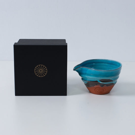 Turquoise blue Japanese matcha bowl with spout "Soku Blue" pottery beside a black gift box with a gold chrysanthemum crest, made in Japan.