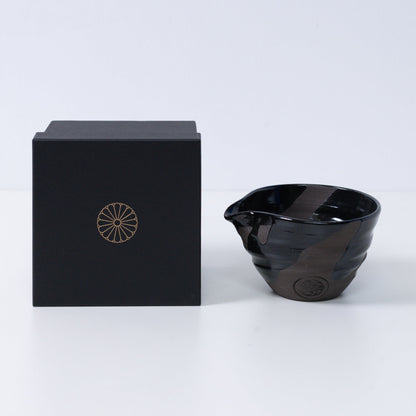 Japanse matchakom met tuit "Sumi Black" aardewerk naast een zwarte geschenkdoos met een gouden keizerlijke chrysant-embleem, keramiek uit Kyoto.
